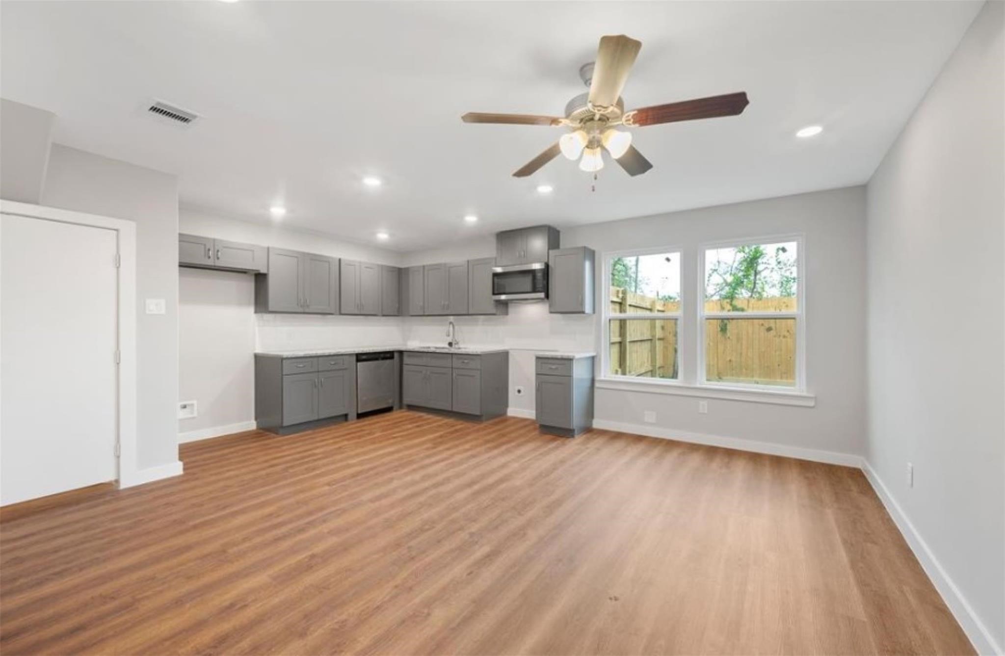 8120 Laura Koppe Road, Unit B Houston, TX 77028 - Photo 3 of 25 A spacious, open-concept kitchen and living area with modern gray cabinets, stainless steel appliances, and wood flooring. The room is brightened by recessed lighting, a ceiling fan, and large windows overlooking a fenced backyard.