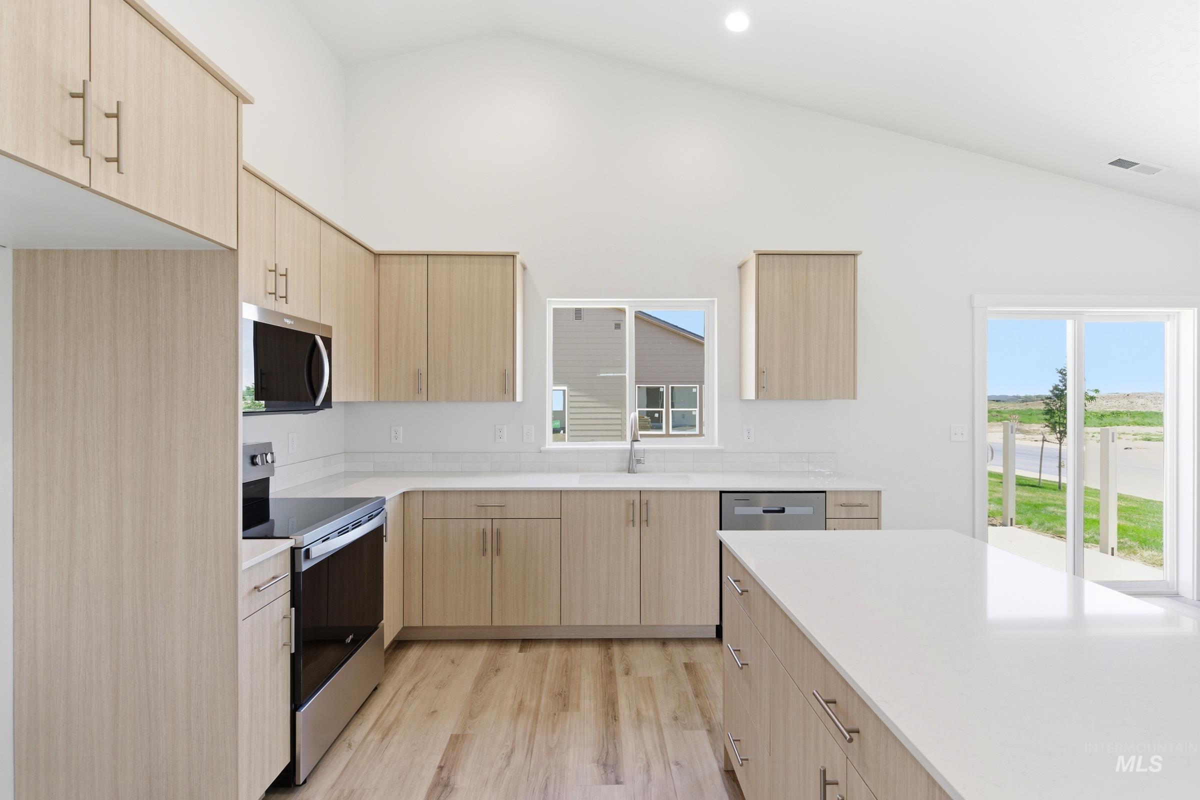 8317 South Tyrion Way Kuna, ID 83634 - Photo 3 of 22 Modern kitchen featuring a vaulted ceiling, wood-finish flooring, light-toned cabinetry with contemporary hardware, stainless steel appliances, and an expansive island with a light-toned countertop
