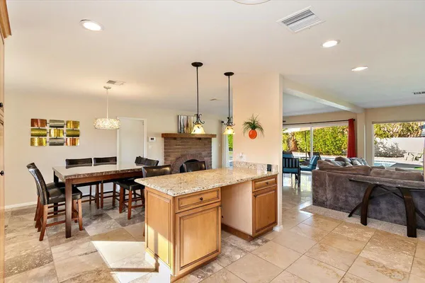 a room with stainless steel appliances kitchen island granite countertop a table chairs and a fireplace