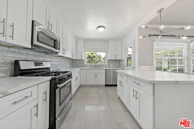 a kitchen with stainless steel appliances granite countertop a stove top oven a sink dishwasher and white cabinets with wooden floor