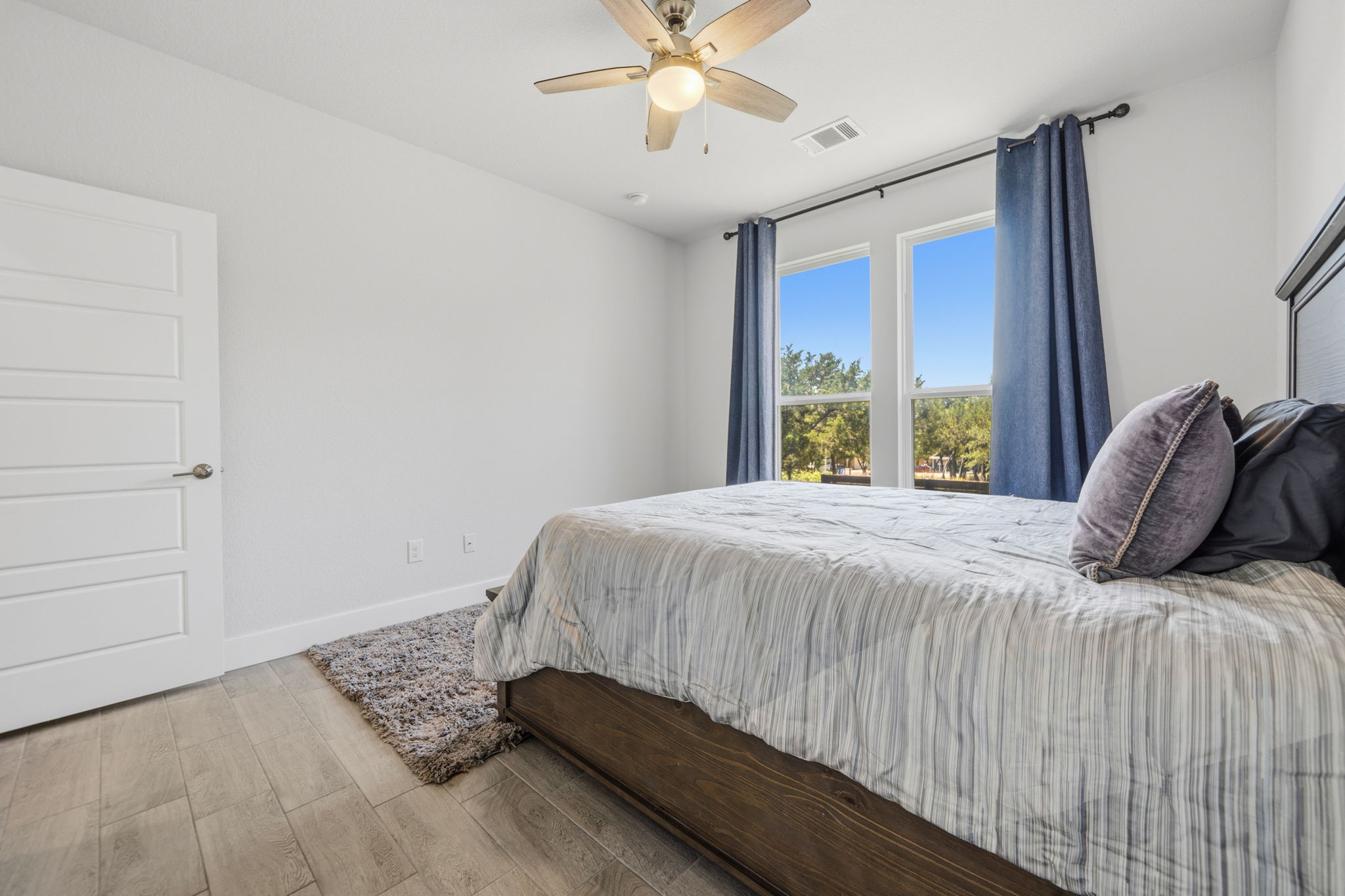 18605 Masters Cove Point Venture, TX 78645 - Photo 24 of 40 Bedroom featuring two large windows, a ceiling fan with integrated lighting, wood-finish flooring, and a five-panel interior door