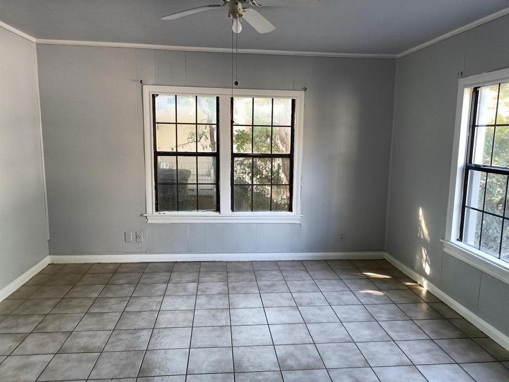 3213 8th Avenue Fort Worth, TX 76110 - Photo 7 of 15 Empty room featuring crown molding, light tile patterned flooring, a ceiling fan, and wood walls