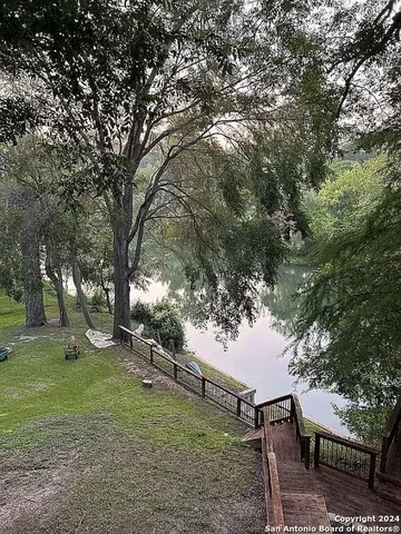 a view of a lake next to a yard with large trees