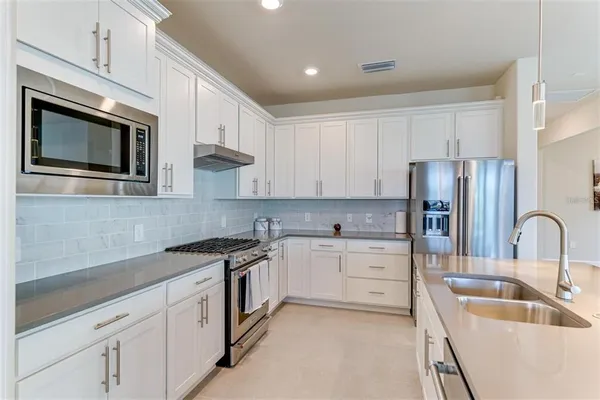 a kitchen with stainless steel appliances granite countertop a sink a stove a refrigerator a microwave oven and white cabinets with wooden floor