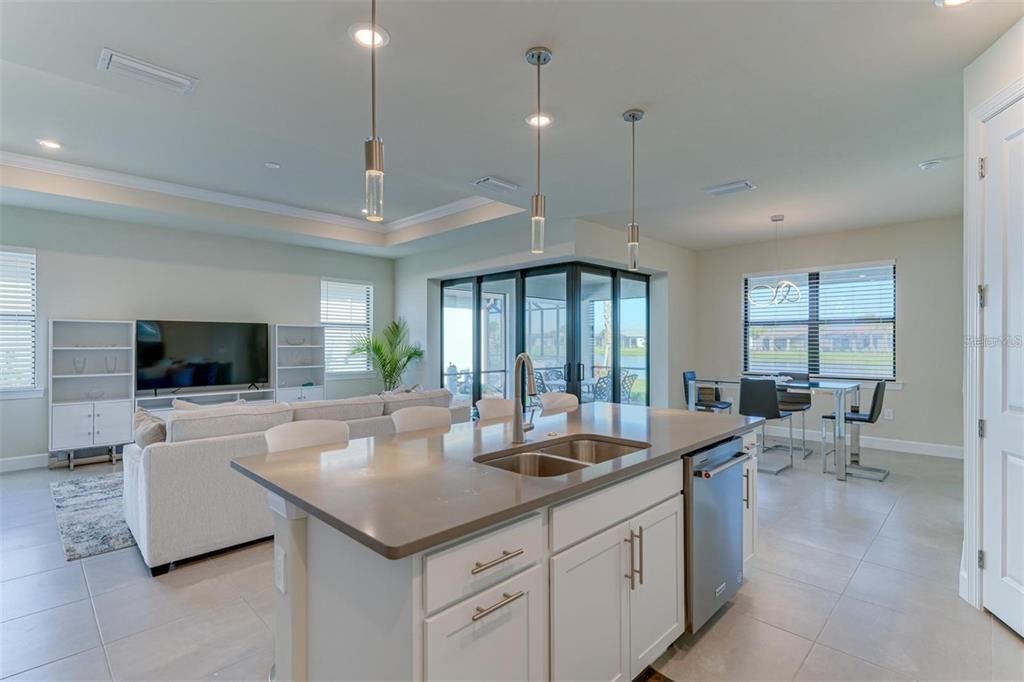 18023 Waterville Place Lakewood Ranch, FL 34202 - Photo 18 of 41 a large living room with stainless steel appliances kitchen island granite countertop a couch and a flat screen tv