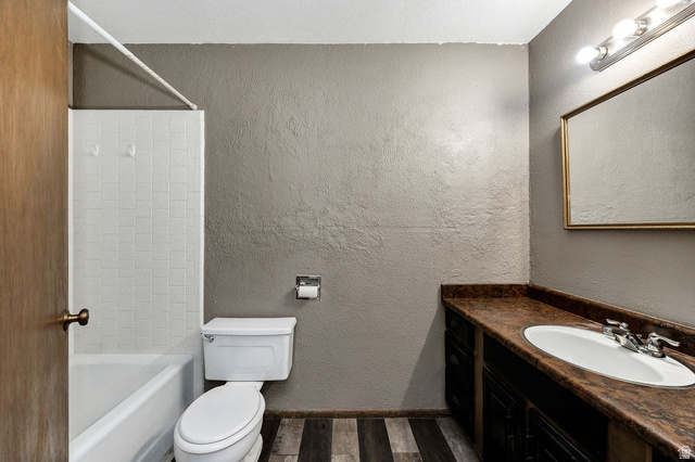 299 West Center Street, Unit 2 Logan, UT 84321 - Photo 27 of 46 Bathroom featuring a white tub and shower surround with tile, a vanity with a white oval sink, a brown patterned countertop, dark wood-finish cabinetry, and wood-finish flooring