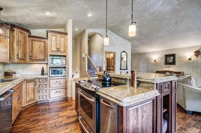 a kitchen with stainless steel appliances granite countertop a stove a sink dishwasher and a refrigerator with wooden floor