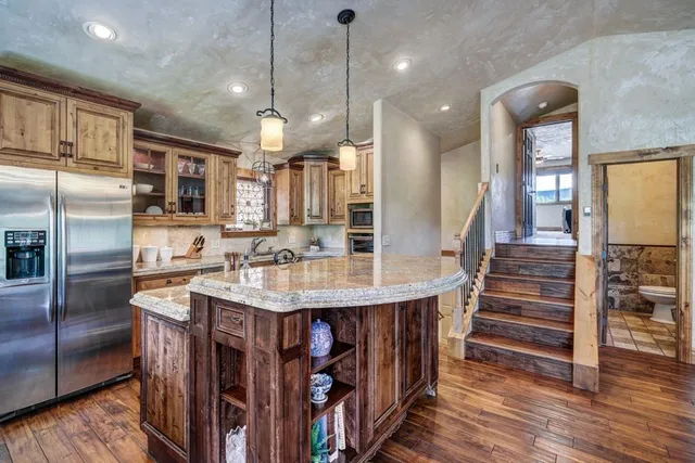 a kitchen with stainless steel appliances granite countertop a kitchen island a stove a refrigerator a oven and a sink with wooden floor