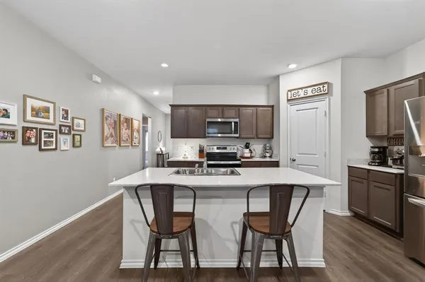 a kitchen with stainless steel appliances granite countertop a dining table chairs refrigerator and sink