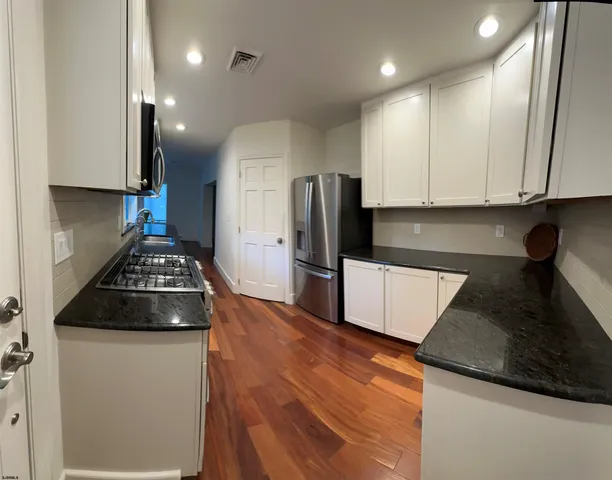 a kitchen with granite countertop stainless steel appliances a stove a refrigerator a sink and white cabinets