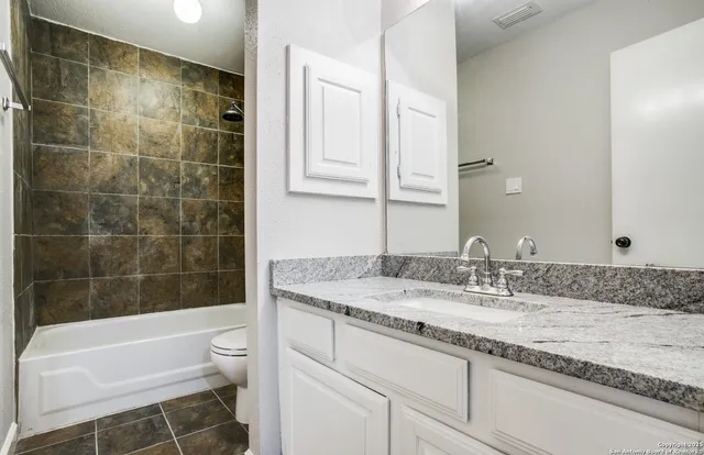 a bathroom with a granite countertop bathtub sink vanity mirror and toilet