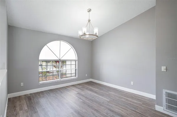 an empty room with wooden floor chandelier and windows