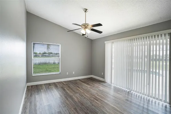 an empty room with wooden floor chandelier fan and windows
