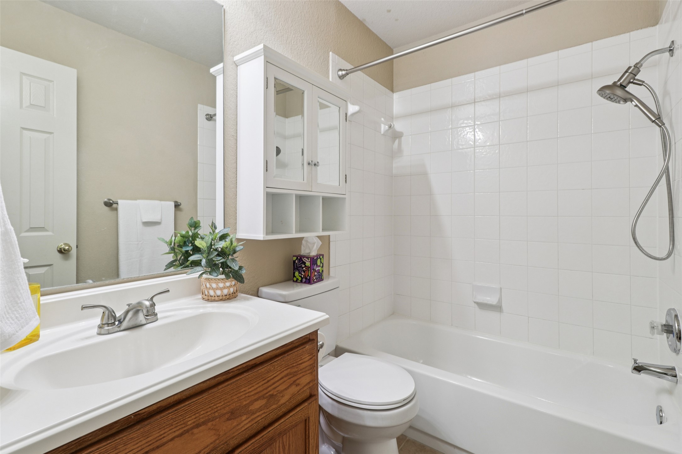 700 Scheel Road Kyle, TX 78640 - Photo 29 of 39 The bathroom features a white bathtub with white tiled walls, a vanity with a white sink and chrome faucet, and a wall-mounted medicine cabinet with glass doors