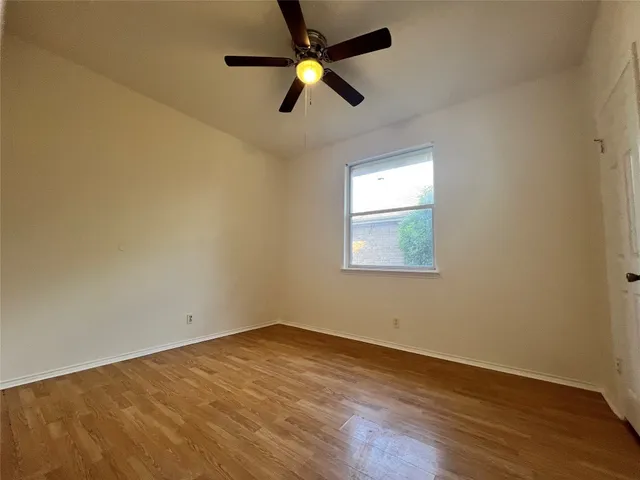 an empty room with wooden floor ceiling fan and windows