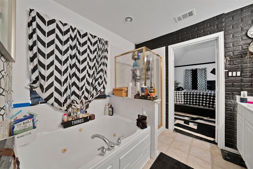 2716 Rochelle Point Irving, TX 75062 - Photo 18 of 40 Soaking tub with jetted features, separate shower enclosure with gold-tone framing, white vanity with integrated sink, and dark textured wall covering