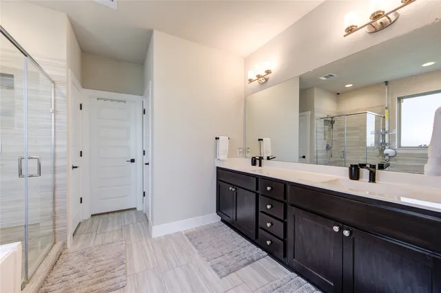 a spacious bathroom with a double vanity sink a large mirror and shower