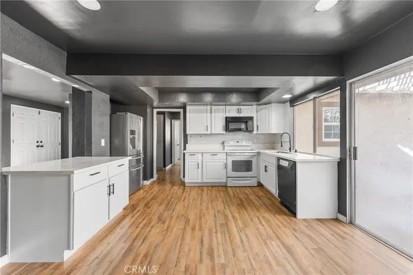 a kitchen with stainless steel appliances a stove top oven a sink dishwasher a refrigerator and white cabinets with wooden floor