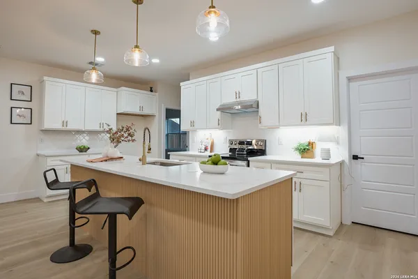 a kitchen with a sink a stove a refrigerator and white cabinets with wooden floor