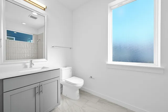 a bathroom with a toilet a sink a mirror a window and vanity