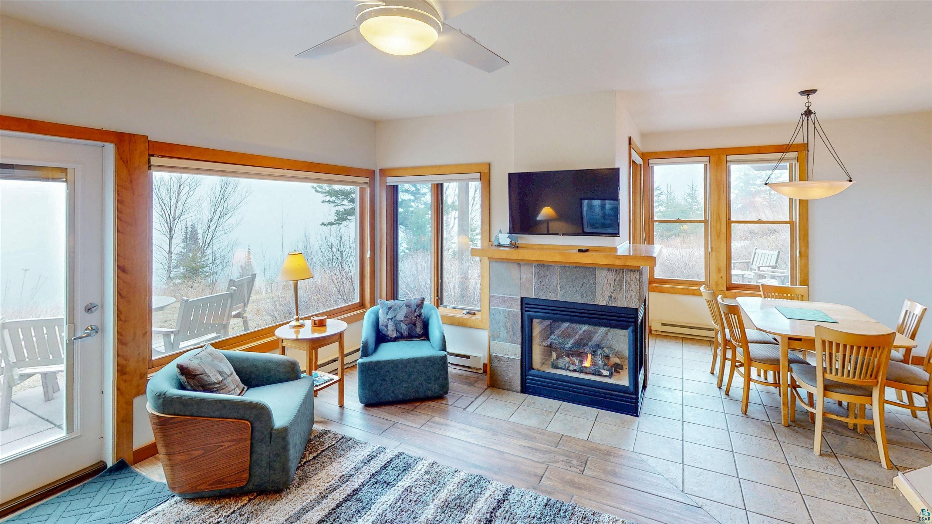 504-506 Poplar River Road, Unit 505 Lutsen, MN 55612 - Photo 4 of 39 Open-concept living area featuring a stone-faced fireplace, large picture windows, wood-finish flooring, a ceiling fan, and a dining area with a contemporary chandelier