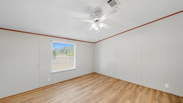 an empty room with wooden floor fan and windows