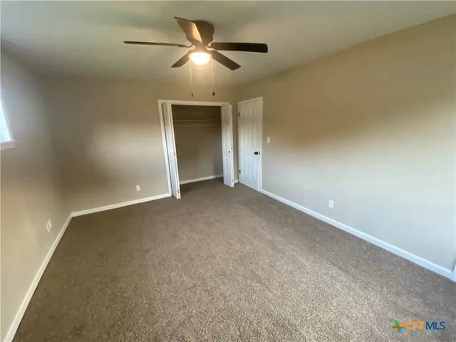 an empty room with chandelier fan and windows