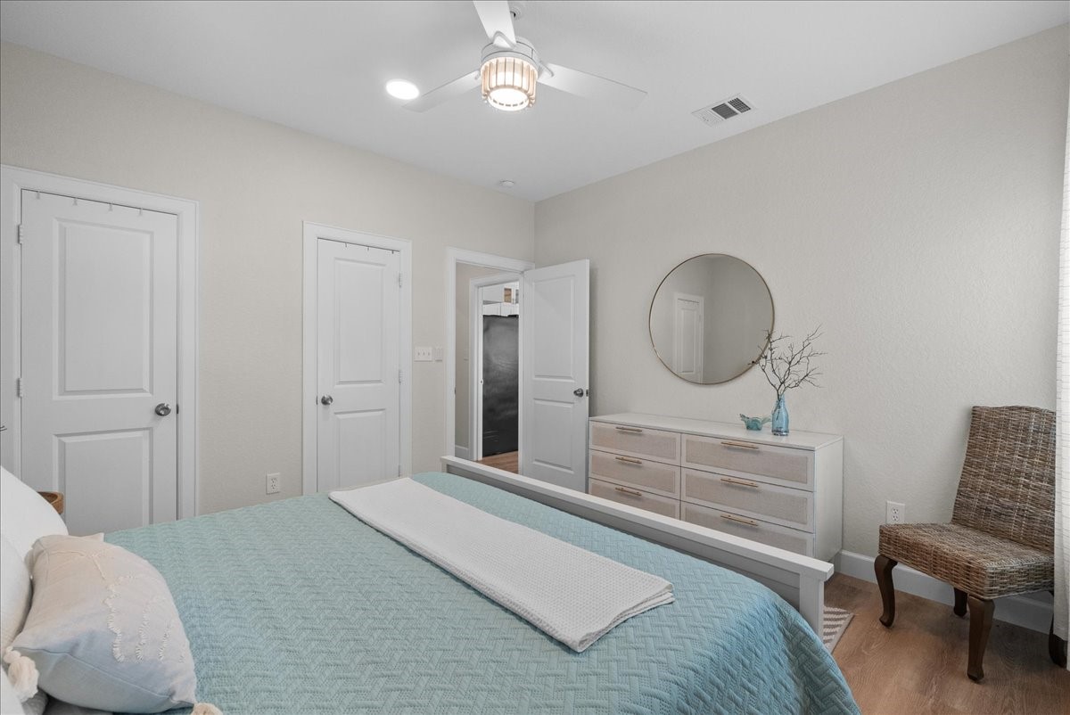130 Beachcomber Avenue Surfside Beach, TX 77541 - Photo 23 of 33 This cozy bedroom features neutral walls, a ceiling fan, and wood look flooring. It includes a comfortable bed, a modern dresser with a round mirror, and a stylish woven chair, offering a blend of functionality and elegance.