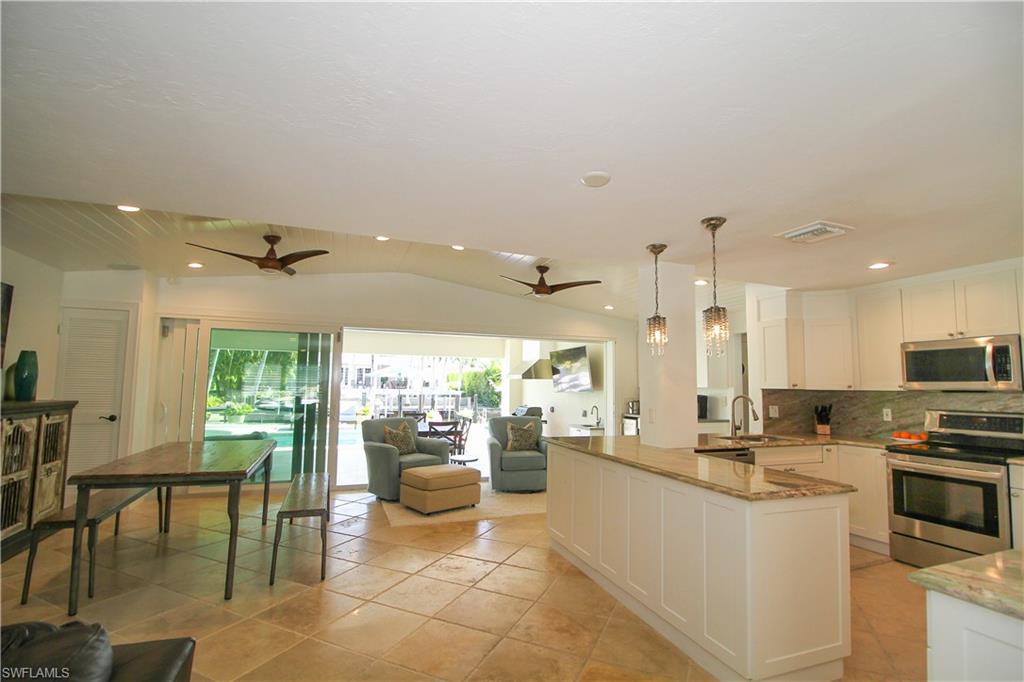 1645 Mullet Court Naples, FL 34102 - Photo 19 of 38 Kitchen with vaulted ceiling, stainless steel appliances, white cabinetry, light stone counters, and hanging light fixtures
