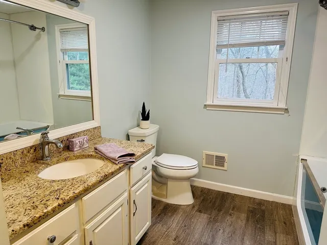 a bathroom with a granite countertop toilet a sink a mirror and a window