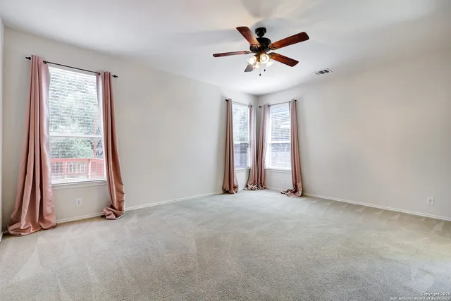 an empty room with ceiling fan and windows