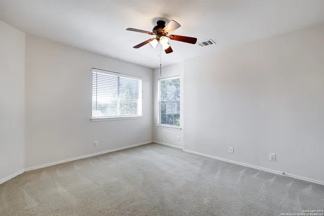 an empty room with ceiling fan and windows