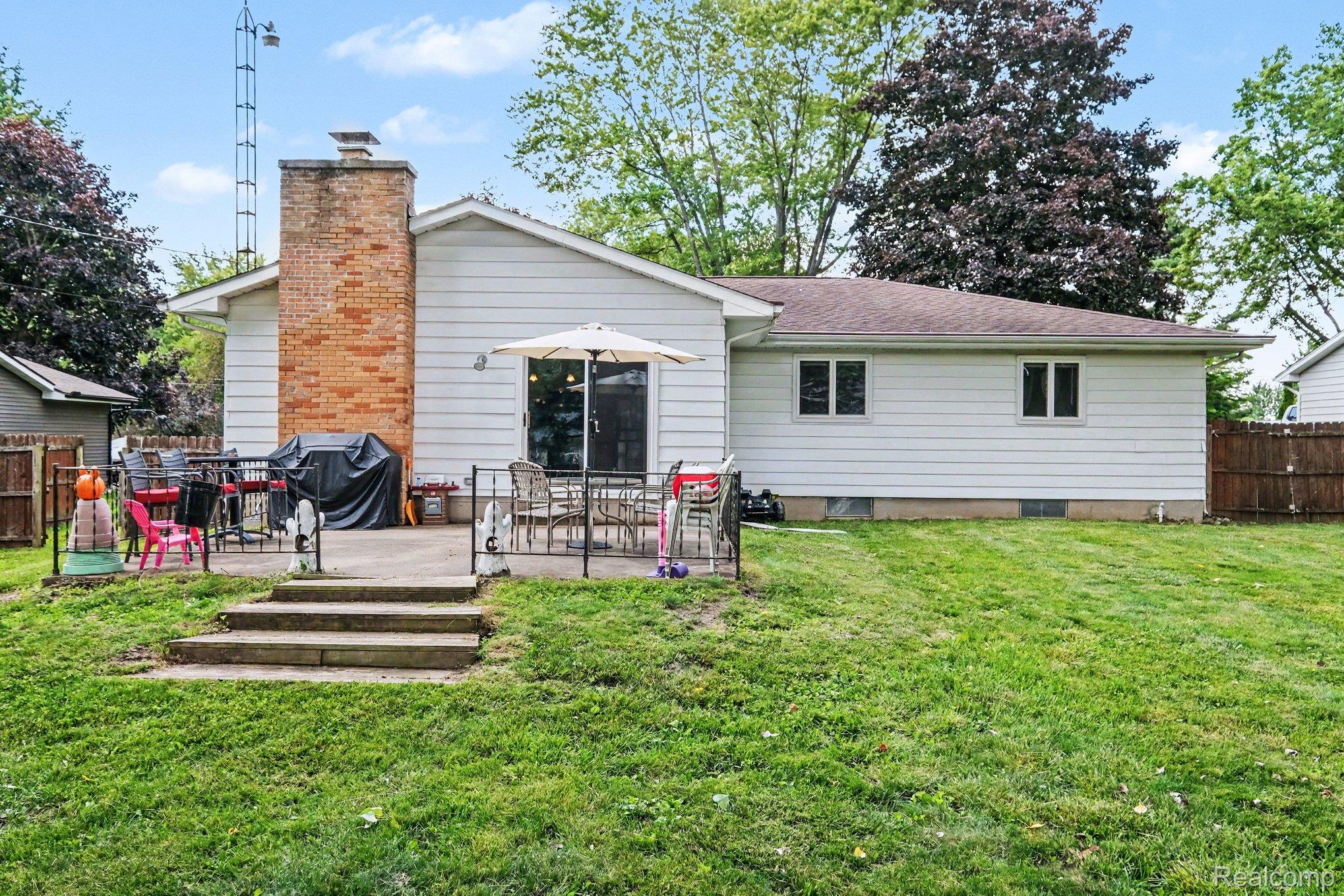 5449 South Genesee Road Grand Blanc, MI 48439 - Photo 16 of 18 Expansive backyard featuring a concrete patio, brick chimney, white siding, sliding glass door, and a partial wood fence