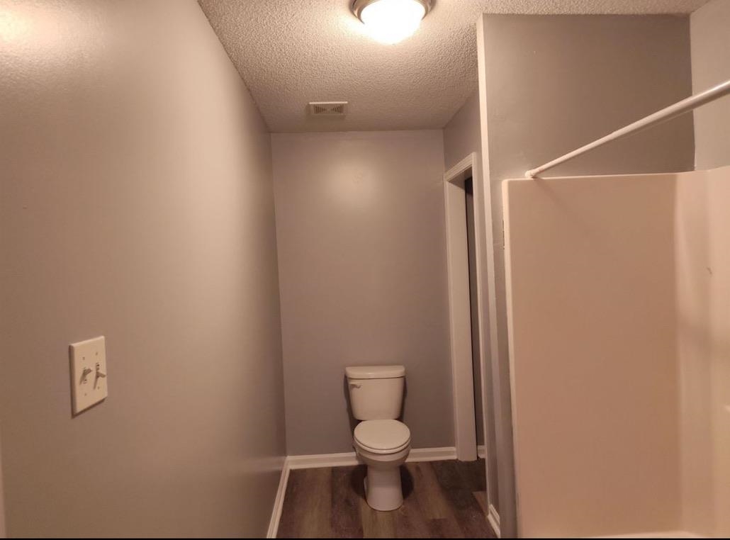 Bathroom with dark wood-style flooring, a textured ceiling, and a shower