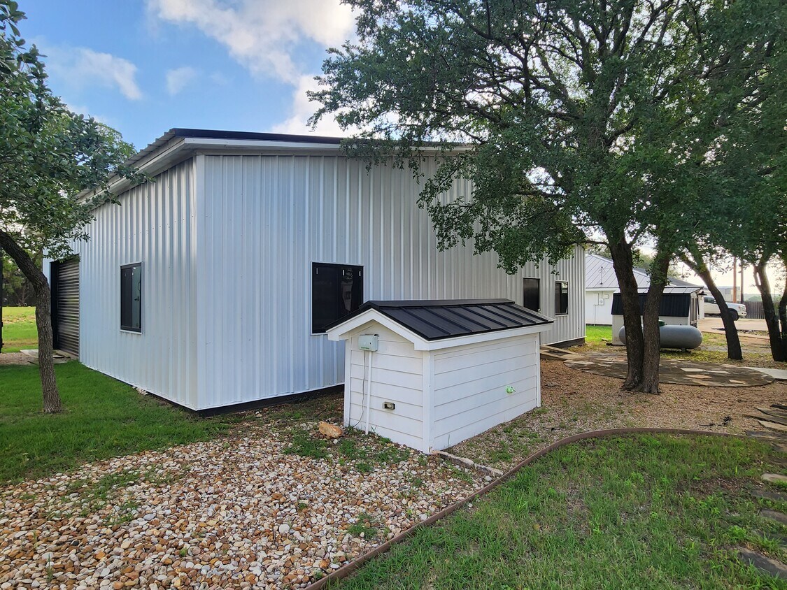 102 County Road 180 Leander, TX 78641 - Photo 15 of 25 A contemporary white metal building with dark-framed windows offers modern functionality in a natural setting.