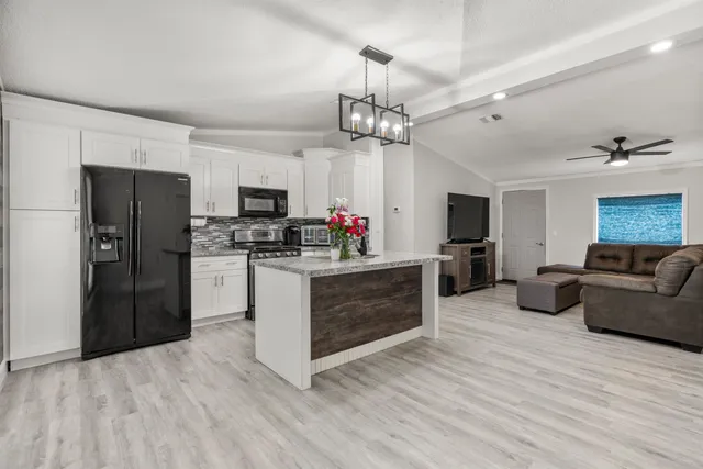 a kitchen with stainless steel appliances kitchen island granite countertop a refrigerator a stove a microwave oven a sink dishwasher and a refrigerator with wooden floor