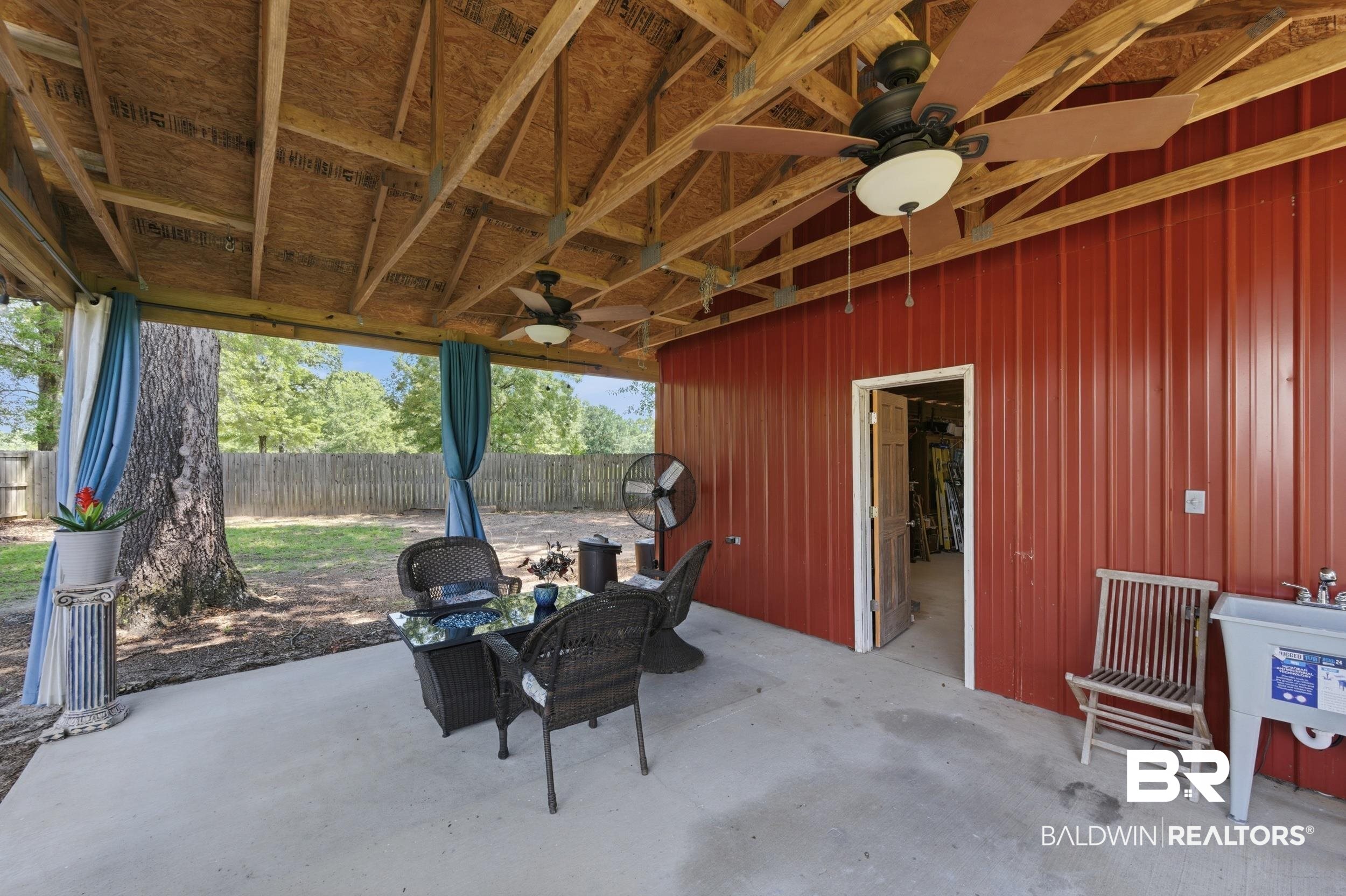 51620 Robert White Road Bay Minette, AL 36507 - Photo 67 of 81 Expansive covered patio featuring a concrete slab, exposed wood beam ceiling, red corrugated metal siding, and two ceiling fans with integrated lighting
