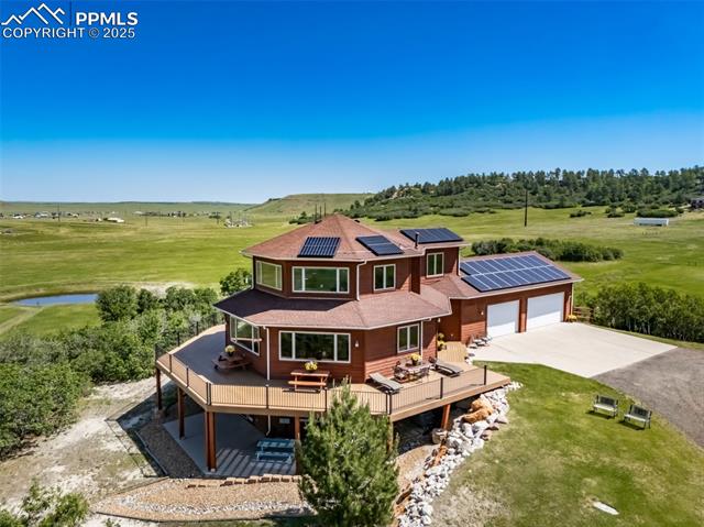 4586 East Best Road Larkspur, CO 80118 - Photo 2 of 50 Rear view of house with a deck, driveway, a patio, solar panels, and a garage