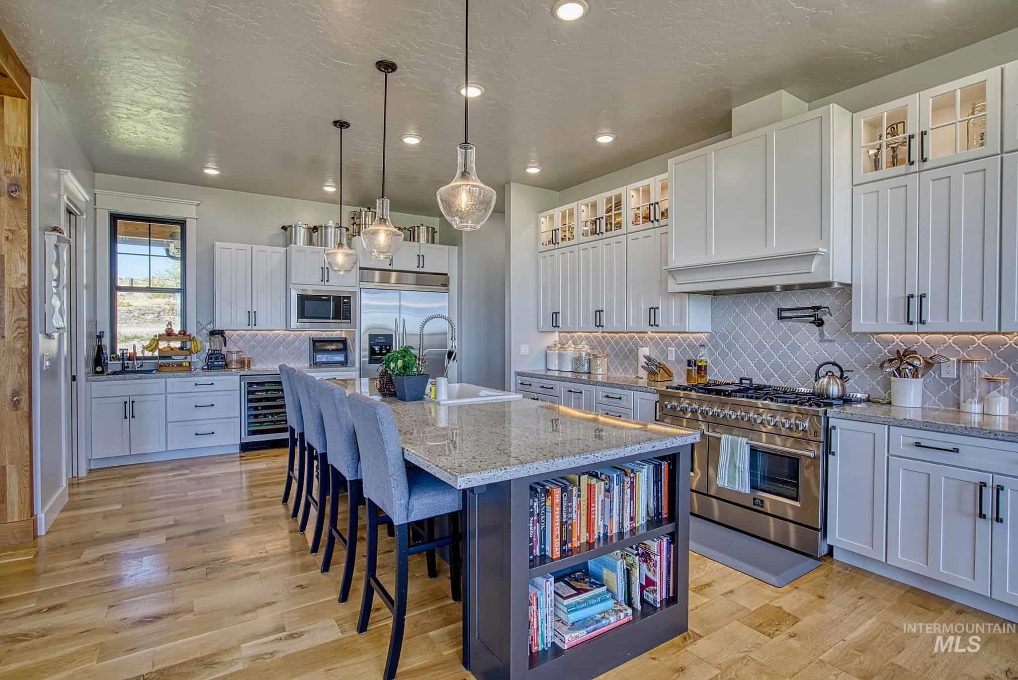 876 Coyote Gulch Road Adrian, OR 97901 - Photo 4 of 50 Spacious kitchen featuring an expansive central island, stainless steel appliances, light-toned cabinetry, wood-finish flooring, and a patterned backsplash