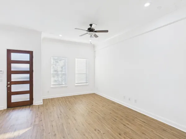 an empty room with wooden floor chandelier fan and windows