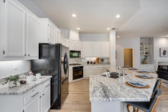 a kitchen with granite countertop kitchen island stainless steel appliances sink refrigerator dining table and chairs