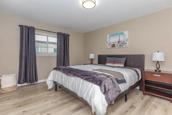 a bedroom with a bed and a lamp on dresser with wooden floor