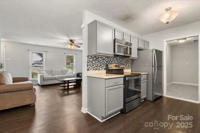 a kitchen with stainless steel appliances kitchen island granite countertop a refrigerator stove and couches with wooden floor