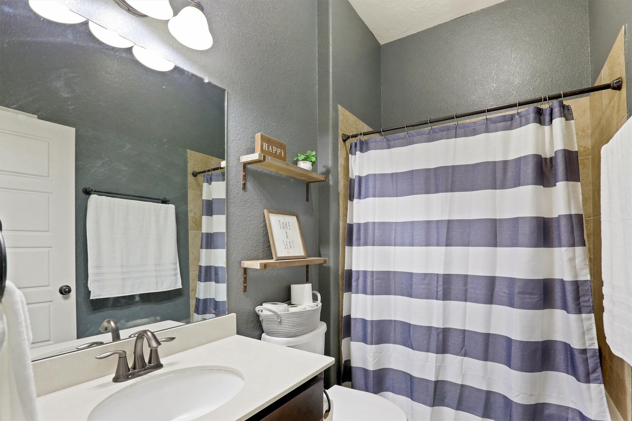 8131 Brinkmeyer Road Needville, TX 77461 - Photo 24 of 49 Charming bathroom with a modern vanity, sleek fixtures, and a stylish striped shower curtain, complemented by warm wall tones and open shelving for added convenience.
