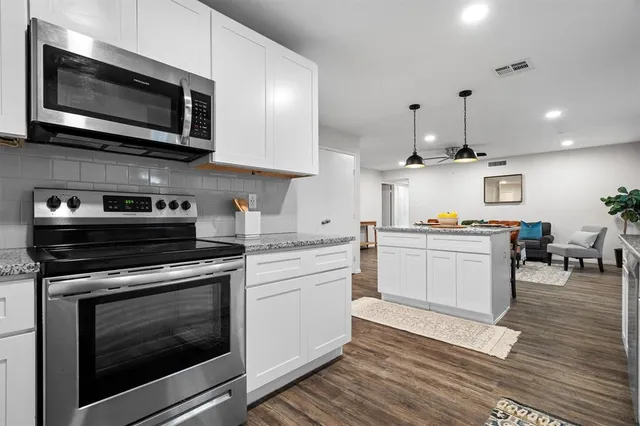 a kitchen with stainless steel appliances white cabinets granite counter tops a stove a sink and a wooden floors