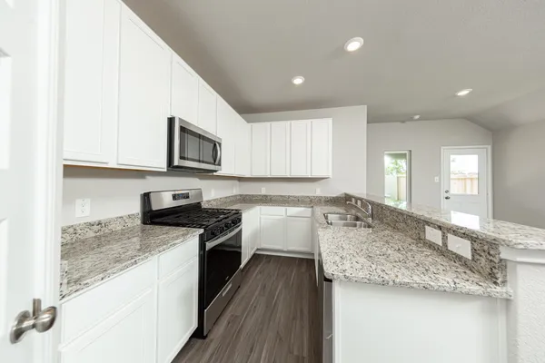 a large kitchen with granite countertop a sink a stove top oven and cabinetry