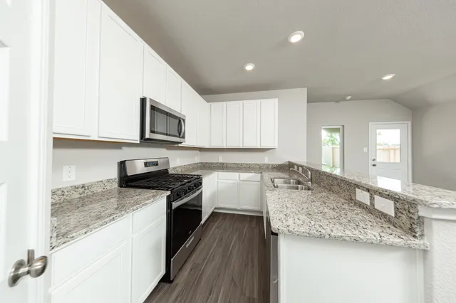 a large kitchen with granite countertop a sink a stove top oven and cabinetry
