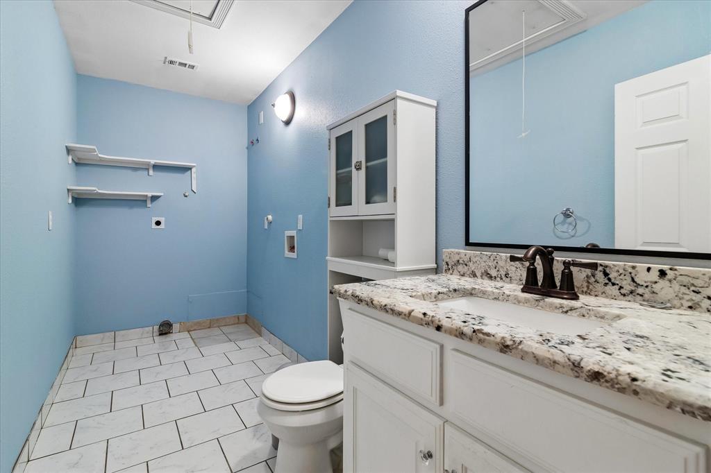 3007 McReynolds Road Sanger, TX 76266 - Photo 28 of 39 Bathroom featuring a granite countertop vanity with an undermount sink and oil-rubbed bronze faucet, white cabinetry, a built-in toilet, tiled flooring, and wall-mounted shelving