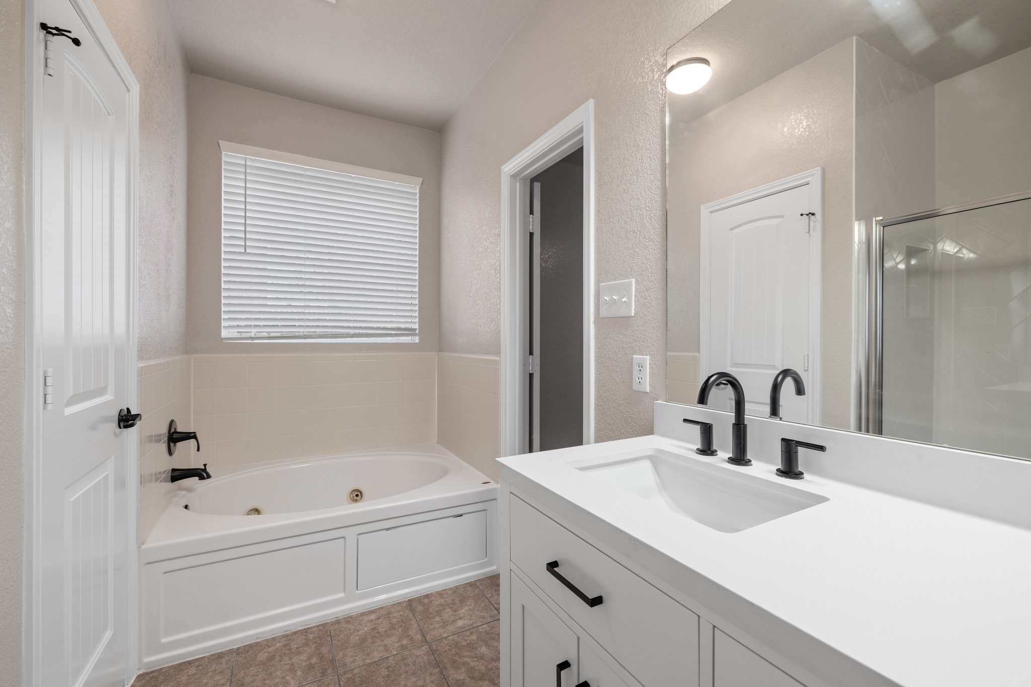 403 Red Hawk Drive Leander, TX 78641 - Photo 17 of 37 Bathroom featuring a soaking tub with black fixtures, a white vanity with an integrated sink, black faucet, and a large wall mirror