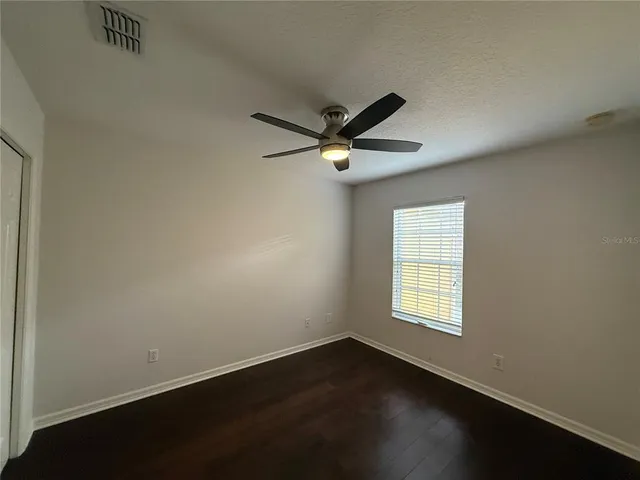 an empty room with wooden floor fan and windows